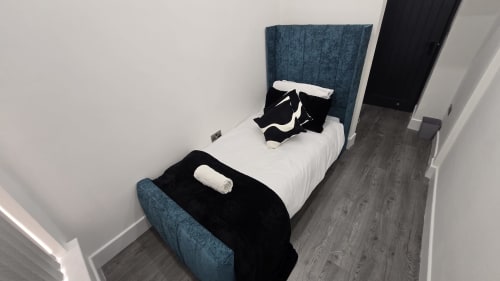 Modern cottage bedroom in Stafford with blue upholstered bed, white linens, black throw blanket, rolled towels, and dark wood