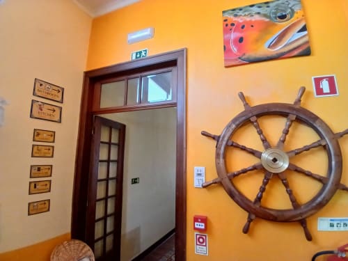 Bright yellow hallway at Bom Caminha hostel in Caminha, Portugal, decorated with nautical theme including ship wheel and fish