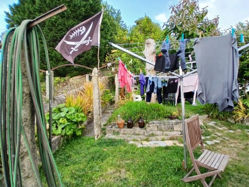 Bom Caminha hostel garden in Caminha with drying clothes, green hose, flag, and potted plants on sunny day