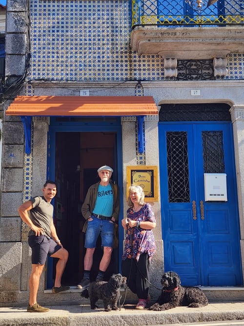 Guests and dogs outside Bom Caminha hostel in Caminha, Portugal, with blue doors and traditional tilework