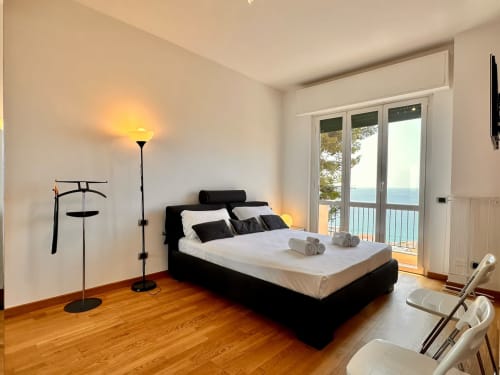 Camera da letto moderna con balcone vista mare, letto nero, pavimenti in legno e arredi contemporanei a Finale Ligure