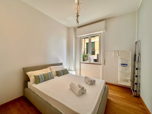 Camera luminosa con balcone vista mare a Finale Ligure, letto bianco con cuscini rigati, pavimento in legno e arredamento moderno