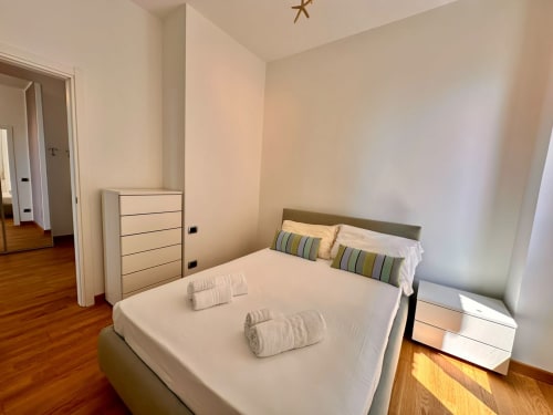 Camera moderna nell'appartamento Il Belvedere, Finale Ligure, con vista mare, letto con cuscini rigati, cassettone bianco, in legno