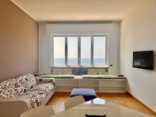 Moderno appartamento a Finale Ligure con vista panoramica sul mare, divano, seduta finestra con cuscini, TV e arredamento in legno