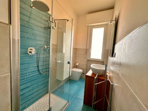 Bagno moderno con doccia in piastrelle turchesi, toilette bianca e lavabo rotondo su vanity in legno al Welcome Holiday, Finale Ligure
