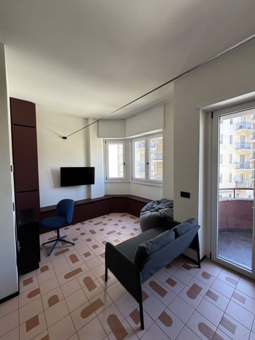Moderno monolocale a Porta Romana Suite Milano con vista città, arredato con divano, sedia da ufficio, TV e accesso al balcone