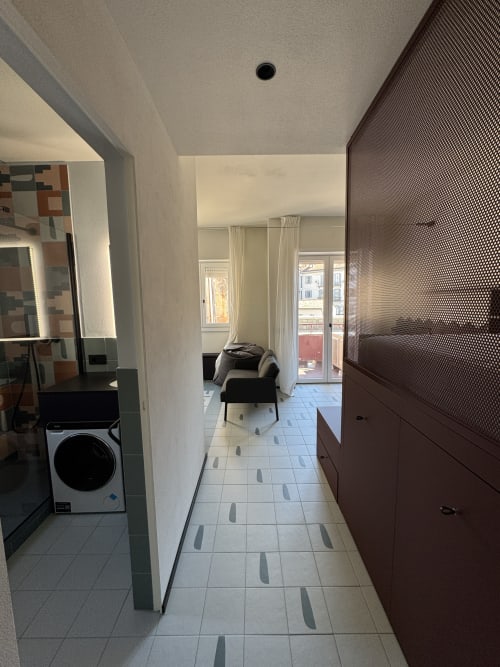 Moderno corridoio della Suite Porta Romana Milano con lavatrice, armadiature scure e zona living adiacente