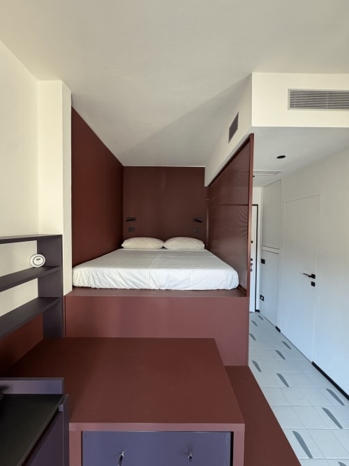 Camera da letto moderna della Porta Romana Suite Milano con letto bordeaux integrato, biancheria bianca e design minimalista