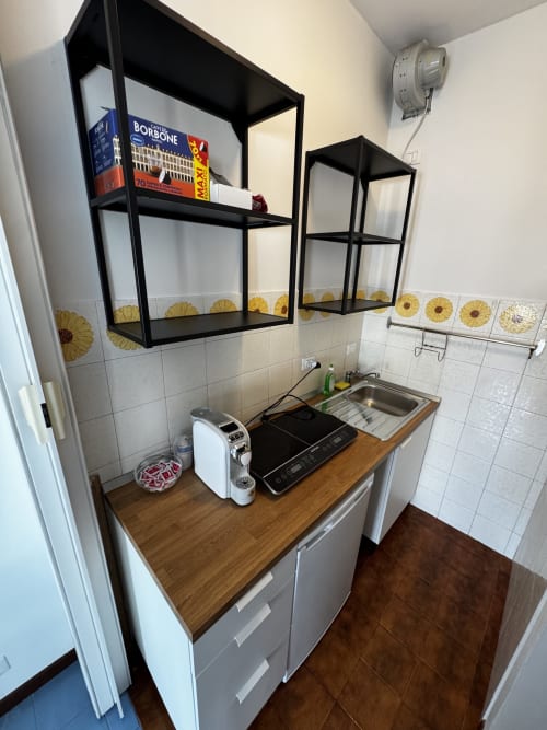 Cucina compatta nella Suite Porta Romana di Milano con scaffali neri, piano di lavoro in legno e motivi girasoli