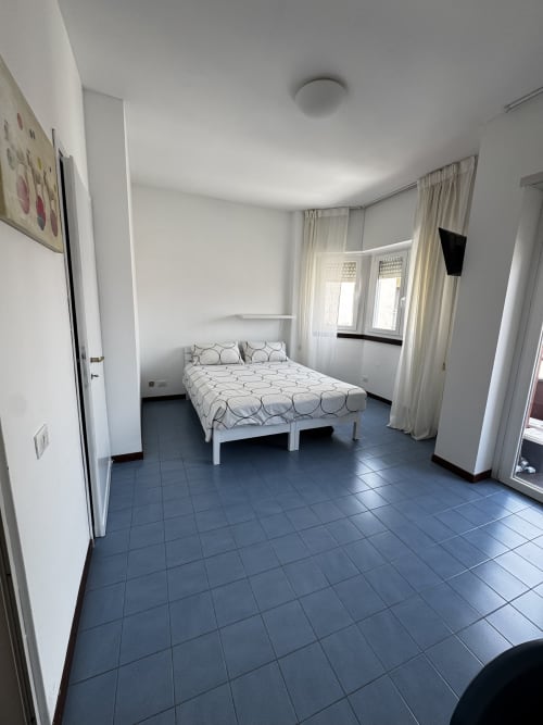 Luminoso monolocale a Porta Romana Suite Milano con letto matrimoniale, pavimento piastrellato blu e ampie finestre con tende trasparenti