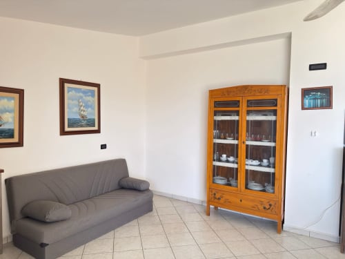 Luminoso loft a Poseidon Bay Residence a Milazzo con divano grigio, mobile da esposizione in legno, arte nautica