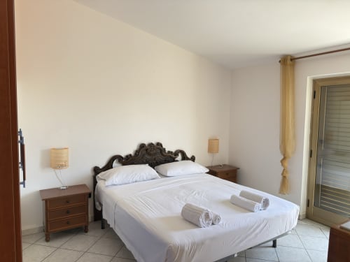 Camera da letto elegante a Poseidon Bay Residence a Milazzo con testata ornamentale, biancheria bianca e arredamento costiero