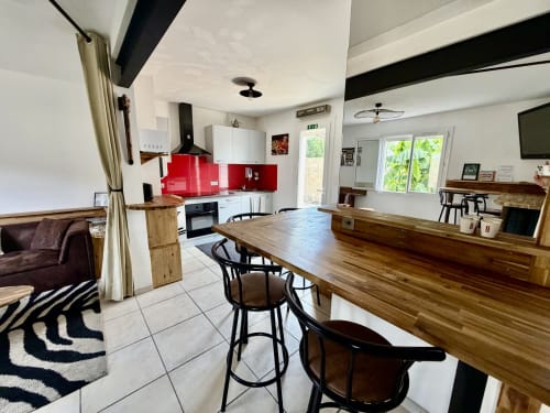 Cuisine ouverte et salon moderne à la Villa des Palmiers avec dosseret rouge, table en bois et vue sur le jardin