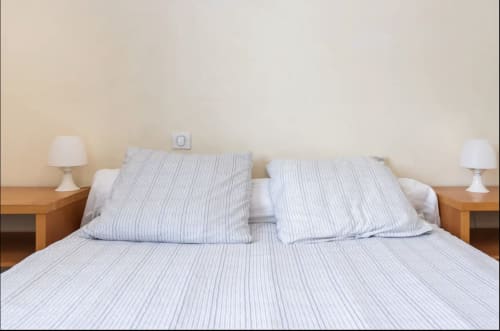 Chambre moderne à la Villa des Palmiers avec coussins rayés, tables de nuit en bois et lampes blanches