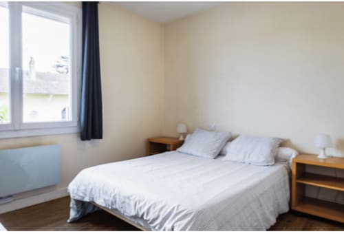 Chambre lumineuse à la Villa des Palmiers avec lit double, tables de nuit en bois et vue sur le jardin à Villeneuve-sur-Lot
