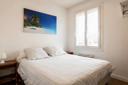 Chambre lumineuse à la Villa des Palmiers B&B à Villeneuve-sur-Lot avec literie blanche, table de nuit en bois et vue tropicale