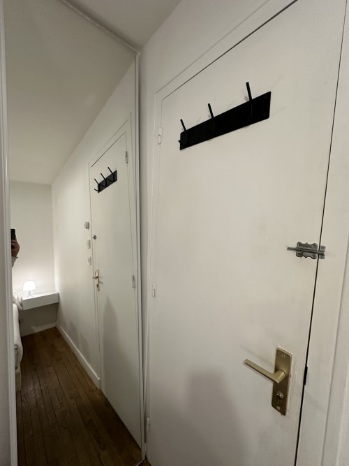 Couloir étroit de la Villa des Palmiers aux murs blancs, sol en bois et crochets muraux noirs à Villeneuve-sur-Lot