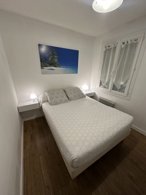Chambre moderne à la Villa des Palmiers avec lit queen-size, lampes de chevet, œuvres d'art marines et vue sur le jardin