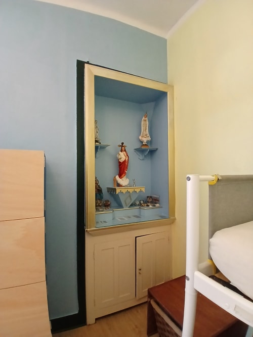 Pequeno santuário religioso no quarto dormitório da pousada Bom Caminha com estátuas e prateleiras