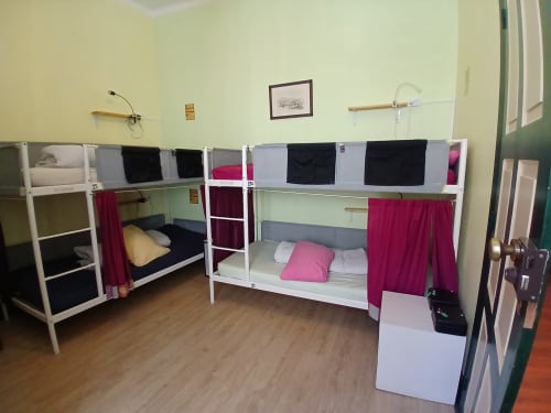 Quarto de dormitório feminino na pousada Bom Caminha em Caminha com quatro beliches brancos, cortinas magenta e piso de madeira
