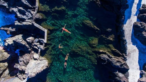 Vista aérea de nadadores em água cristalina turquesa nas piscinas naturais de Porto Moniz, Portugal