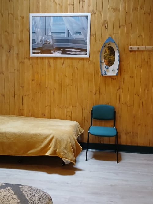 Chambre double à l'auberge Bom Caminha avec murs en bois, lit avec jeté doré, chaise bleue et œuvre marine