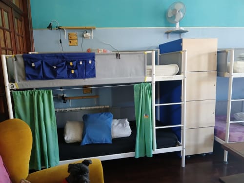 Dortoir mixte de 12 lits à l'auberge Bom Caminha à Caminha avec lits superposés, rideaux verts, étagères de rangement et bleu
