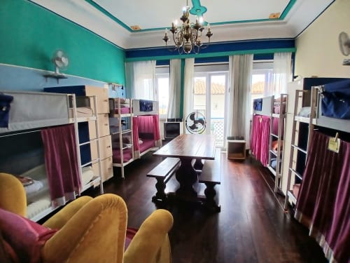 Dortoir mixte de 12 lits à l'auberge Bom Caminha avec lits superposés, murs turquoise, parquet et coin salon partagé