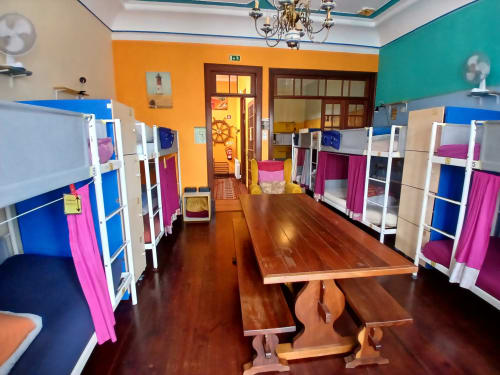 Colorful 12-bed mixed dormitory at Bom Caminha hostel in Caminha, Portugal, featuring bunk beds with pink curtains and wooden