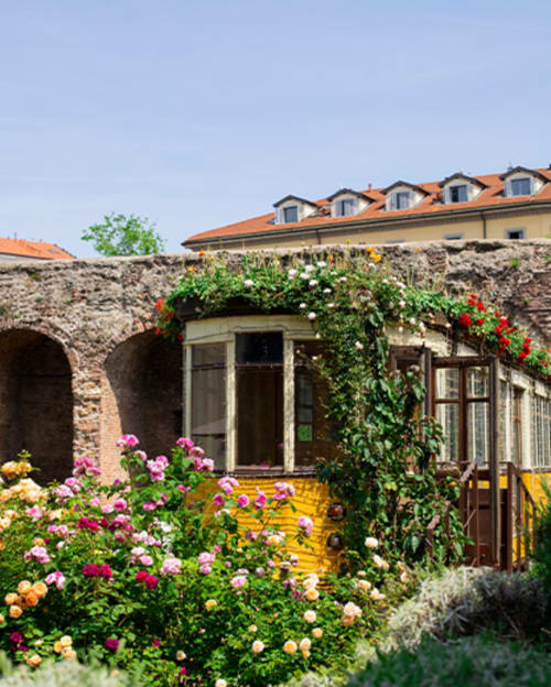Cortile della Porta Romana Suite Milano con rose in fiore, archi in pietra e ingresso cottage giallo