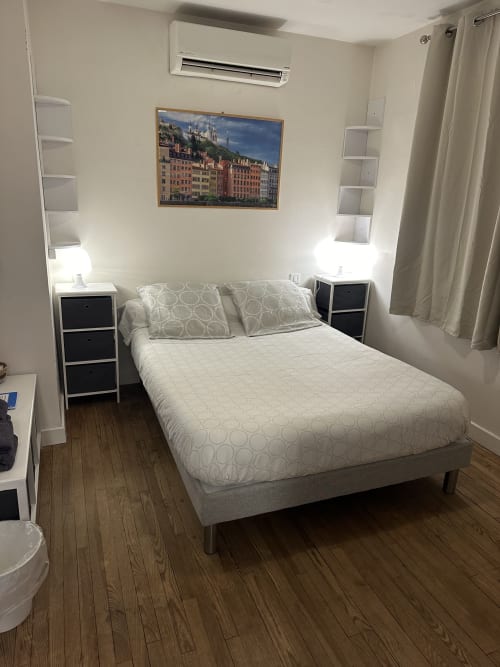 Chambre moderne à la Villa des Palmiers avec lit queen-size, tables de nuit blanches, climatisation et tableaux de paysages urbains européens