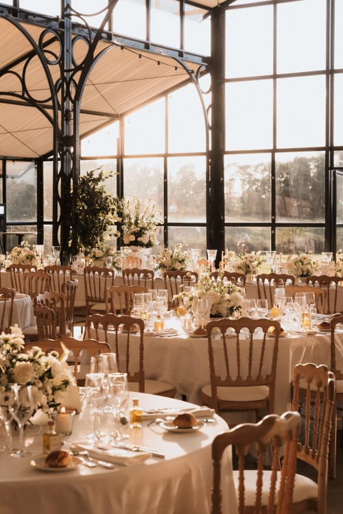 Réception de mariage élégante au Domaine Du Réveillon avec linges crème, chaises en bois et arrangements floraux blancs en verre