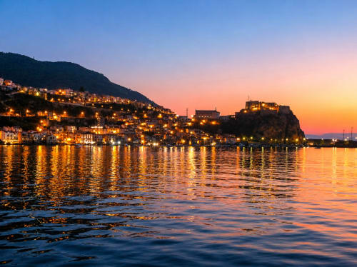 Lungomare di Reggio Calabria al tramonto, edifici illuminati sulla collina riflessi nelle acque tranquille