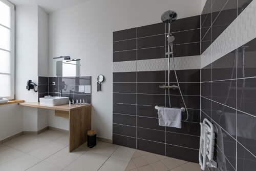 Salle de bains moderne de la chambre supérieure de l'Hôtel Le Château avec carrelage à rayures noires, vasque en bois et douche à l'italienne