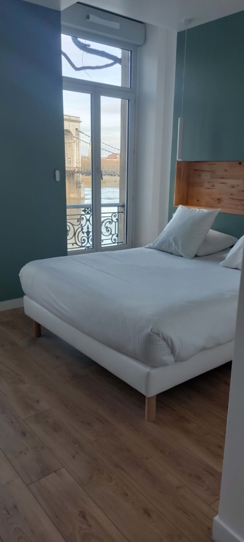 Chambre moderne à l'Hôtel Le Château avec lit double, balcon vue rivière, murs d'accent bleu-vert et parquet