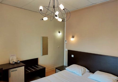 Chambre double à l'Hôtel Le Château avec tête de lit noire, literie blanche, lustre et équipements modernes