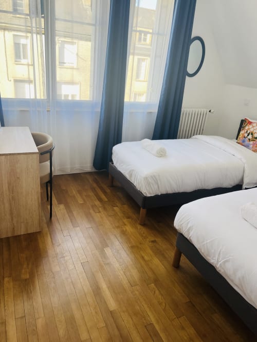 Deux lits jumeaux aux draps blancs dans la chambre Carterret de La villa Cassinne à Montebourg, avec vue sur la ville et rideaux bleus