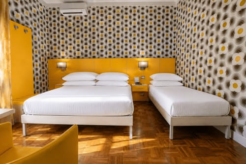 Camera moderna del B&B Pellicano con due letti, testata gialla, pareti decorate e pavimento in legno a Reggio Calabria