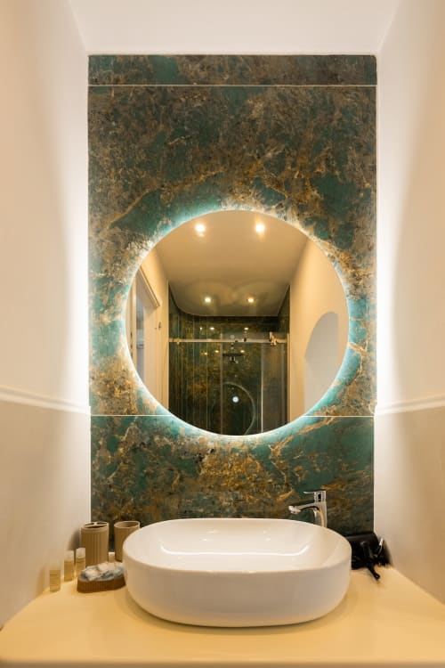 Bagno ecologico a Origenes Rooms, Procida con specchio circolare illuminato, parete in marmo e lavabo bianco