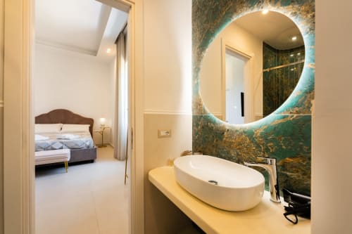 Bagno moderno con specchio ovale illuminato e lavabo in marmo nella camera Eco di Origenes Rooms, Procida, con vista sul mare e collegamento
