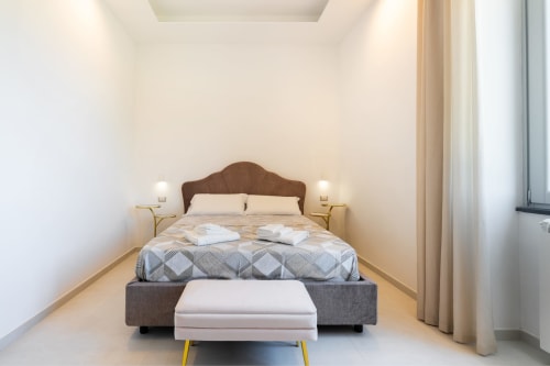 Camera moderna presso Origenes Rooms a Procida con letto testata marrone, biancheria bianca, arredamento neutro e vista mare