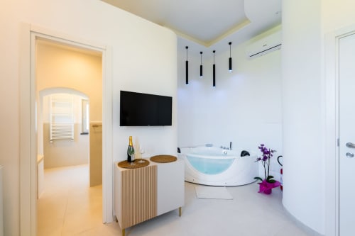 Moderno bagno spa con vasca idromassaggio bianca, TV, luci a sospensione e vista mare presso Origenes Rooms a Procida