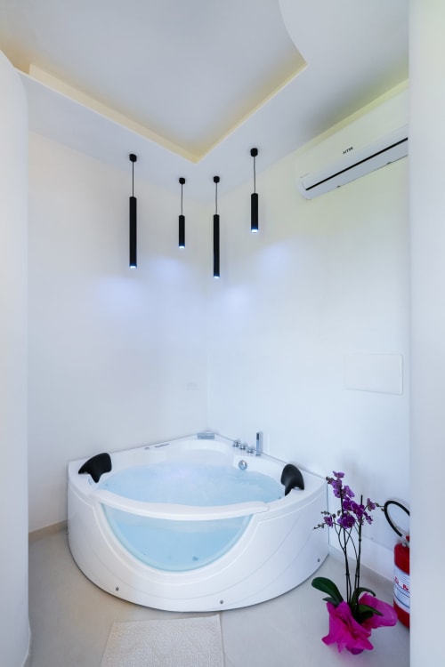 Bagno moderno con vasca idromassaggio angolare bianca, lampade a sospensione nere, climatizzatore e fiori viola