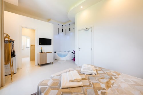 Camera moderna con vasca idromassaggio a Origenes Rooms, Procida, con vista mare, biancheria geometrica beige e design contemporaneo