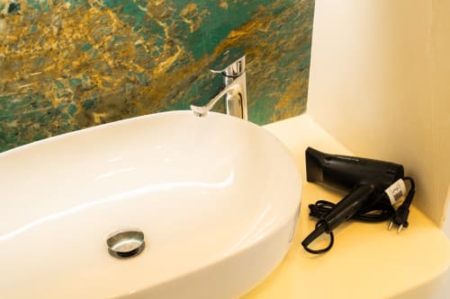 Lavabo bianco con rubinetto cromato, asciugacapelli e specchio nella camera del B&B di Procida con rivestimento in marmo verde
