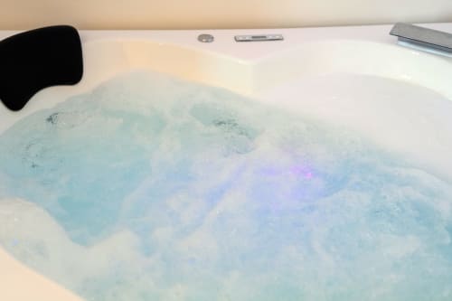 Vasca idromassaggio con acqua turchese frizzante e illuminazione viola in una camera Eco presso Origenes Rooms, Procida