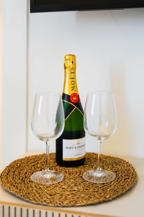 Bottiglia di champagne Moët & Chandon con due calici su sottopiatto intrecciato presso Origenes Rooms, Procida
