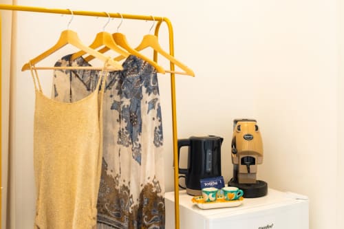 Camera Eco di Origenes Rooms, Procida: appendiabiti giallo con abbigliamento e macchina da caffè su scaffale bianco