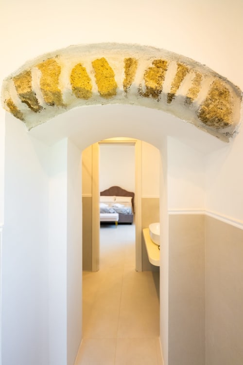 Arco d'ingresso nella camera B&B di Procida con muri imbiancati e dettagli dorati che conduce alla camera da letto