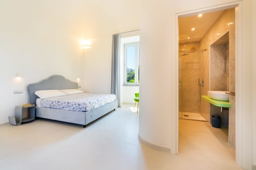 Camera moderna presso Origenes Rooms a Procida con vista mare, pavimenti in marmo e bagno privato con doccia walk-in